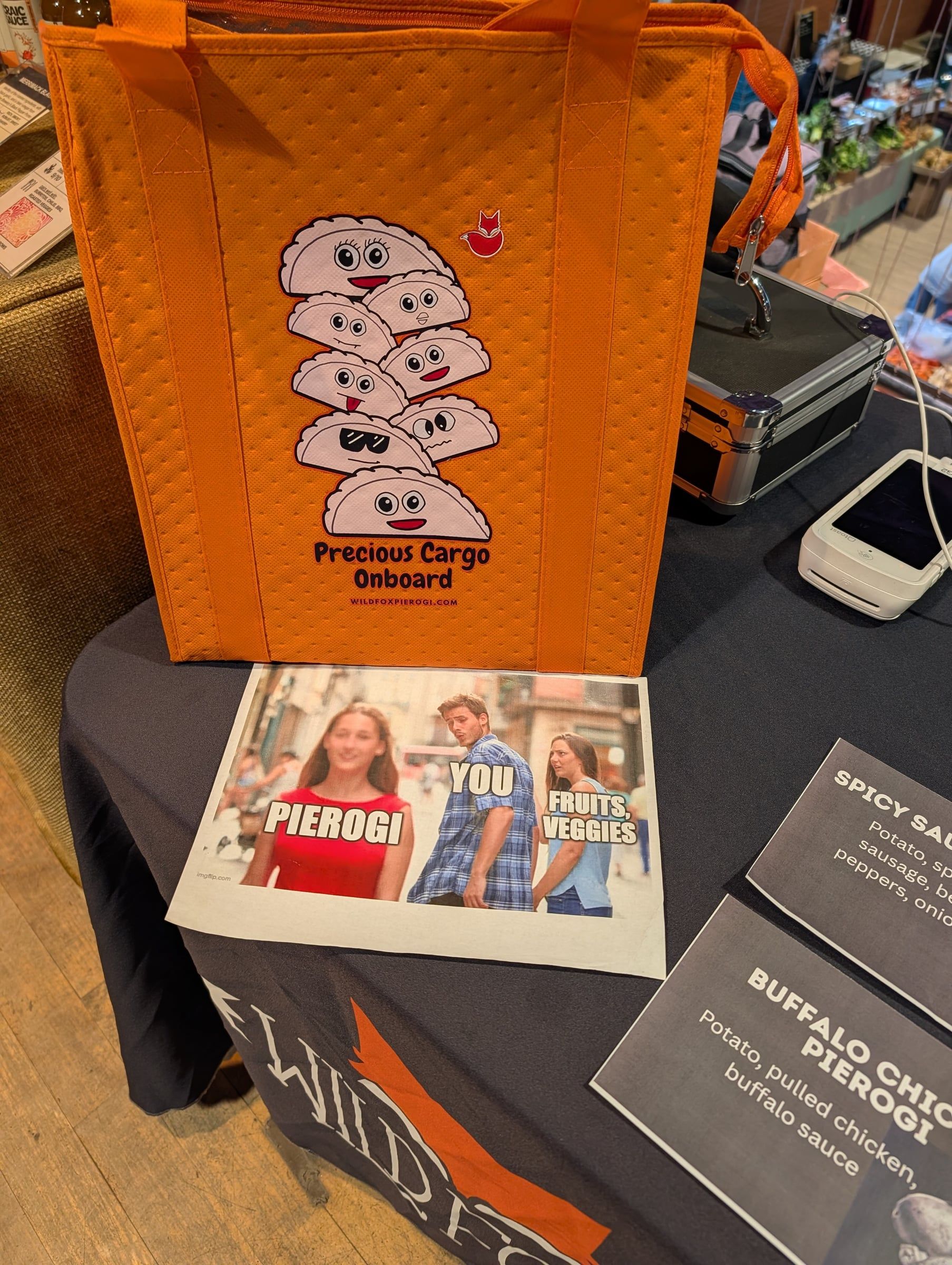 An orange "Precious Cargo Onboard" pierogi tote and a pierogi meme on the market table